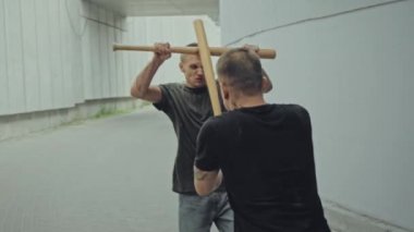 Beyzbol sopalı iki adam beton duvarların yanında kavga ediyor. 