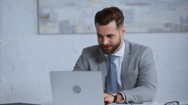 Ofiste dizüstü bilgisayar kullanan takım elbiseli neşeli bir işadamı. 