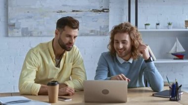 Mutlu iş adamları kağıt bardağın yanındaki dizüstü bilgisayara bakıyor. 