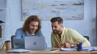 Kâğıt bardağın yanında dizüstü bilgisayara bakan neşeli iş adamları 