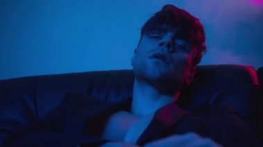 Yakışıklı adam dumanla mavi kameraya bakıyor.