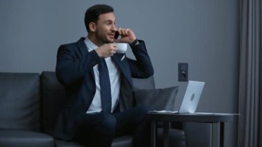 Mutlu iş adamı akıllı telefondan konuşuyor ve kahve içiyor. 