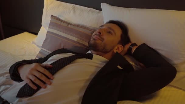 穿着西服的快乐商人躺在旅馆房间的床上 — 图库视频影像