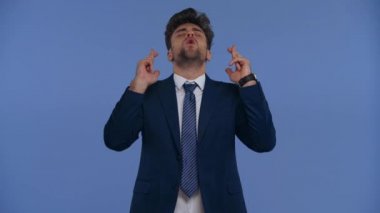 Parmaklarını çapraz yapıp evet diyen bir iş adamı mavi üzerine izole edilmiş bir hareket yapıyor.