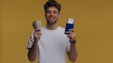 Elinde para, pasaport ve uçak bileti olan gülümseyen adam sarıya izole edilmiş.