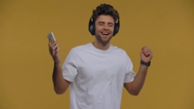 Kulaklıklı mutlu adam akıllı telefon tutuyor ve sarıda tek başına dans ediyor.