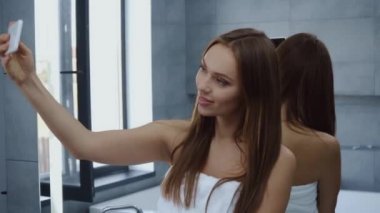 Banyoda selfie çeken banyo havlusu giymiş güzel bir kadın.