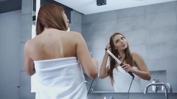 漂亮的年轻女子在浴室里梳着卷曲的铁头 — 图库视频影像