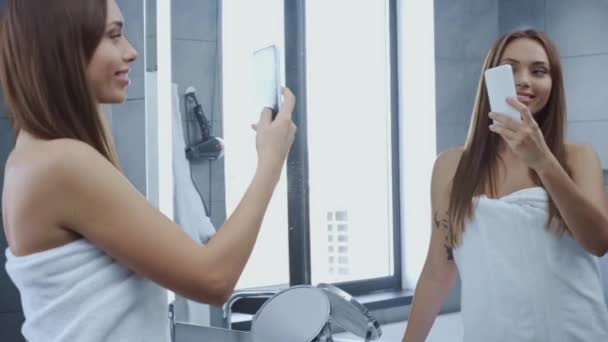 穿着浴巾的漂亮而快乐的年轻女人在浴室的镜子里拿着自己的东西 — 图库视频影像