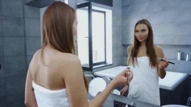 Güzel genç bayan banyo havlusu içinde aynanın önünde kozmetik fırça kullanıyor.