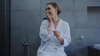 Mutlu genç bir kadın banyoda pozitif hamilelik testine bakıyor.