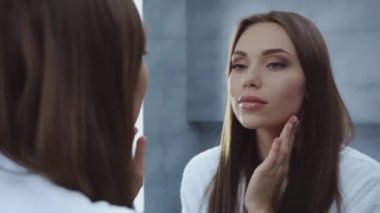 çekici genç bir kadın aynanın karşısında yüzüne dokunuyor.