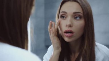 Bornozlu genç bir kadın aynaya bakıyor.