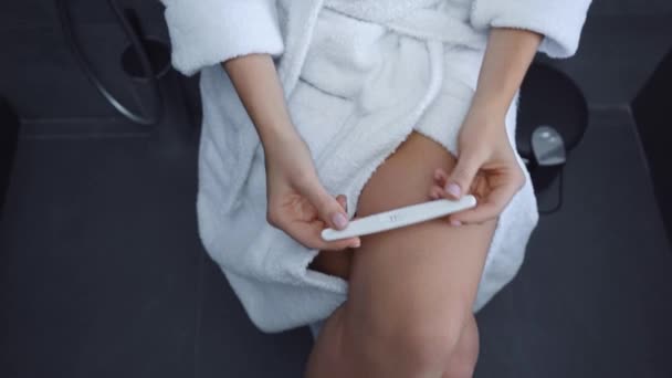 陽性の妊娠検査を受けたバスローブの若い女性のクロップドビュー — ストック動画