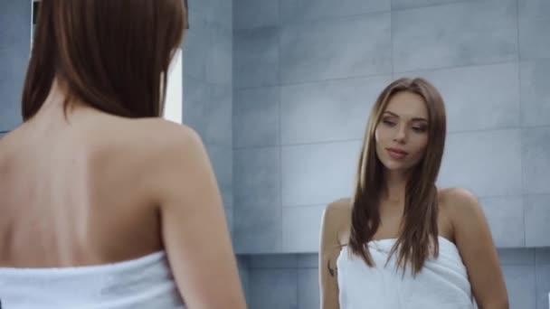 在浴室里 穿着浴巾的年轻漂亮女人在镜子前摸着头发 — 图库视频影像