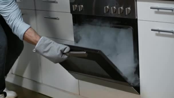 台所用手袋の男のクロップドビューオープンキッチンでオーブン喫煙 — ストック動画