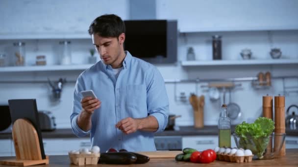 Jovem Homem Ler Receita Smartphone Olhando Para Ingredientes Mesa — Vídeo de Stock