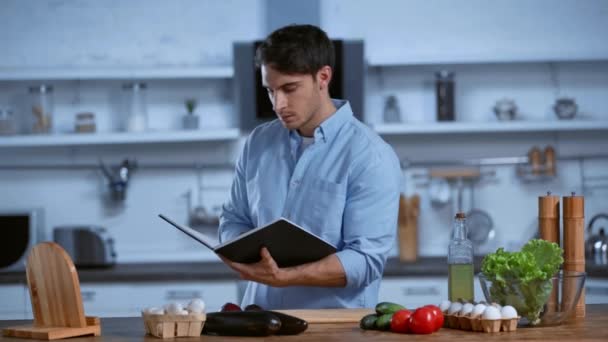 Hombre Leyendo Libro Cocina Mientras Está Pie Cerca Mesa Con — Vídeo de stock