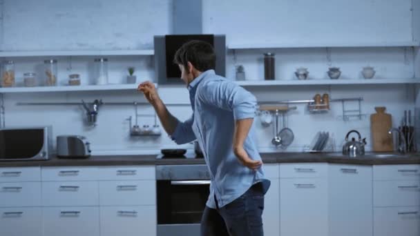 穿着蓝色衬衫的快乐男人在现代宽敞的厨房里跳舞 — 图库视频影像