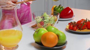 Mutfak masasındaki taze salataya zeytinyağı ekleyen kadın manzarası.