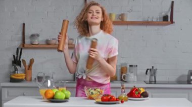 Biber ve tuz değirmenleriyle gülümseyen kız salatanın yanında dans ediyor.
