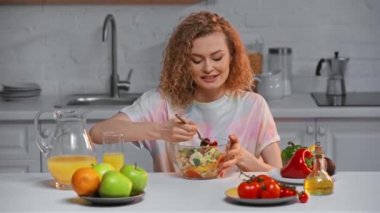 Mutfak masasında taze salata yiyen neşeli kadın. 