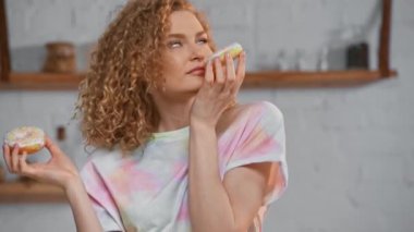 Neşeli kız donut kokluyor ve kameraya bakıyor.