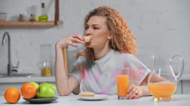 Gülümseyen kadın donut yiyor ve mutfakta portakal suyu içiyor. 