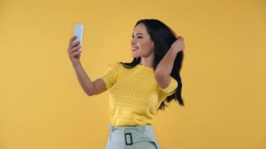 Sarıda izole edilmiş akıllı telefonlu çekici bir kadın selfie çekiyor.