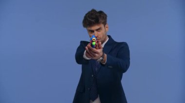 Oyuncak tabancayla oynayan yakışıklı iş adamı mavi üzerine izole edilmiş.