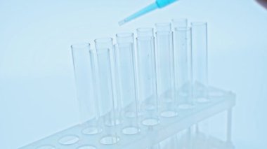 Bilim adamının deney tüplerine pipetle mavi aşı eklediği görüntüler.