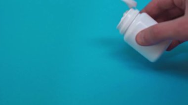 Turkuaz yüzeyine kavanozdan haplar döken adamın görüntüsü.