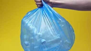 Kırpılmış görüntüde elinde plastik şişelerle çöp torbası tutan adam var.