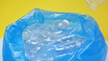 Kırpılmış insan görüntüsü plastik şişeleri sarı poşete koyuyor. 
