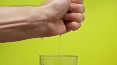 Erkek eli, yeşil, yavaş çekimde izole edilmiş bardakta limon suyu sıkıyor.