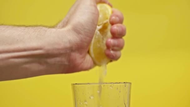 黄色のスローモーションで隔離されたガラスの中にレモンジュースを絞る男性の手 — ストック動画