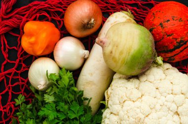 Siyah arka planda, yeniden kullanılabilir kırmızı ağ torbası üzerinde taze sebzeler. Organik hasat. Sıfır atık alışveriş kavramı. Üst görünüm