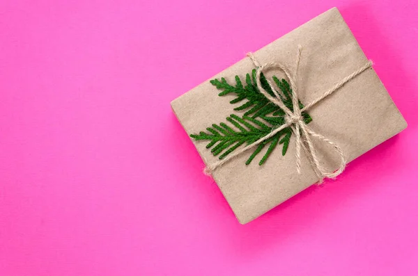 礼品盒，用牛皮纸包裹，用线捆扎，并在粉红色的背景上用绿色的冷杉枝条装饰。 假期的概念。 死了现在的想法。 平躺在床上 复制空间 — 图库照片