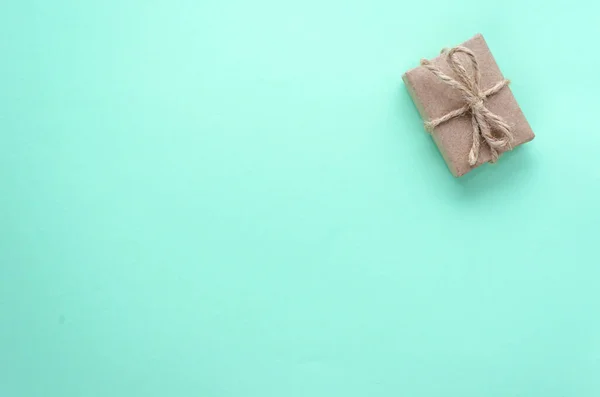 单个礼品盒，用褐色牛皮纸包裹，用细绳绑在浅蓝色的背景上。 礼物的概念。 死了现在的想法。 平躺在地上，尽收眼底。 复制空间 — 图库照片