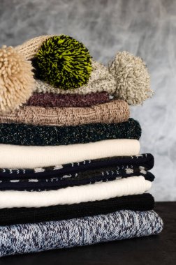 Gri arka planda düzgünce katlanmış kış eşarpları ve şapkalar yığını. Saç giyme mevsimi. Isınma zamanı. Yakın çekim.