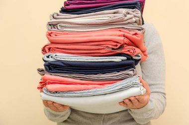 Bej bir arka planda katlanmış temiz bir yatak yığını tutan kadın eller. Ev kavramı. Yakın plan.