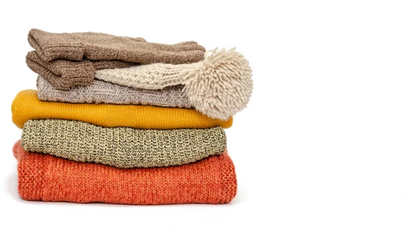 A stack of folded knitted warm women sweaters, hat and gloves on a white background. Season of warm clothes. Time to keep warm. Closeup. Copy space — Stock Photo, Image