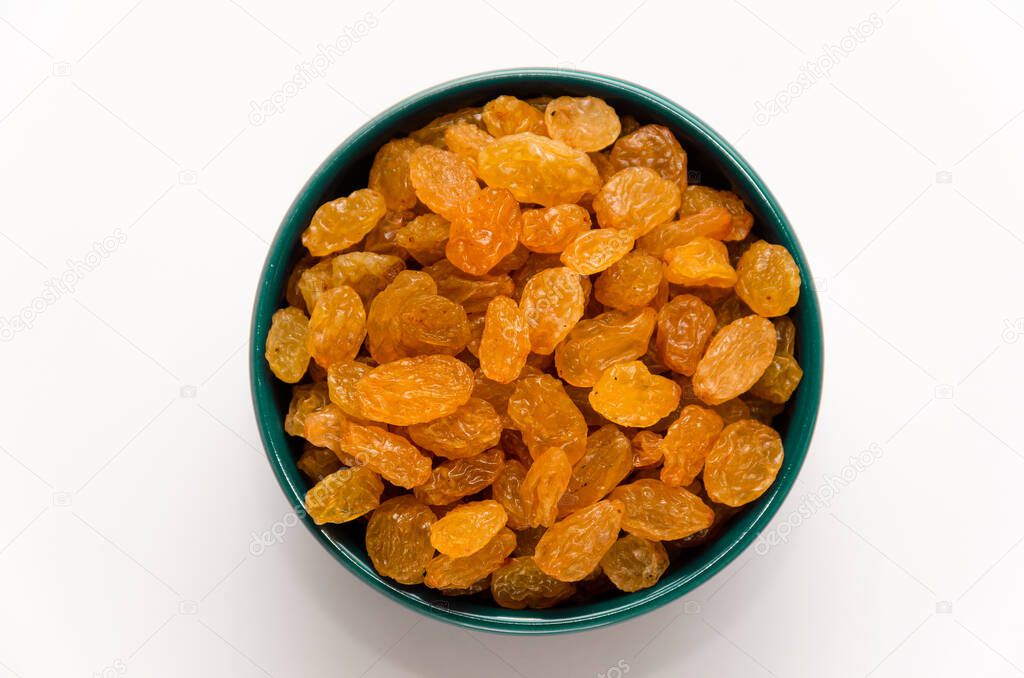 White or golden raisins in a blue ceramic bowl on a white background. Healthy sweets concept. Closeup. Top view