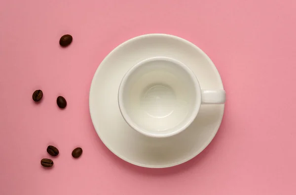 Empty clean white coffee cup on saucer and some coffee beans on millennial pink background. Minimal style. Morning, breakfast, drink coffee concept. Template for feminine blog, social media, networks — Stock Photo, Image