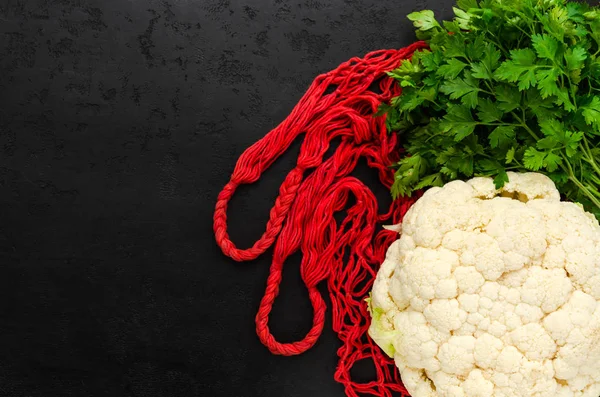 Bolsa de malla de hilo de algodón, coliflor blanca cruda, perejil verde fresco sobre fondo negro. Reutilizable eco amigable bolsa de compras para comestibles. Cero residuos, sin concepto plástico. Asiento plano, vista superior. Copiar espacio — Foto de Stock