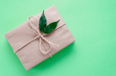 Kraft kağıdına sarılı hediye kutusu. Nane arkaplanında iki yeşil yaprakla sicimle süslenmiş. Diy. Sıfır kayıp tatil konsepti. Düz yatıyordu. Boşluğu kopyala