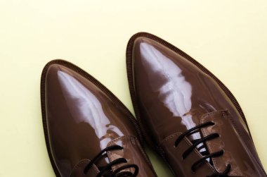 Pastel açık sarı arka planda kahverengi kadın deri ayakkabılarının yakın çekimi. Moda blogu, dergi, güzellik konsepti. Minimum bileşim. Düz yatış, üst görünüm