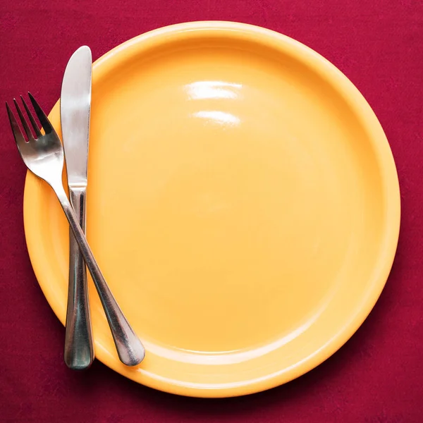 Garfo e faca na placa amarela vazia na toalha de mesa marrom. Vista superior, close-up — Fotografia de Stock