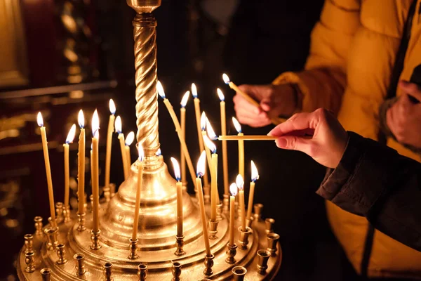 Hands of praying people lighting candles in Christian church. Concept of faith in God. Religious scene. Close-up