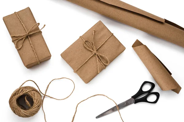 Geri dönüşümlü kağıda sarma işlemi. Hediye kutuları, sicim, kahverengi kağıt rulosu ve beyaz arka planda makas. Eko tarzı. Diy ve sıfır atık konsepti. Düz yatıyordu. Üst görünüm